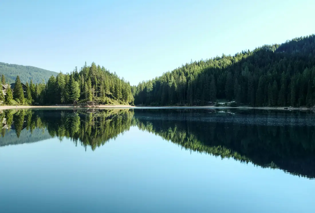 A calm lake reflecting forest and sky.