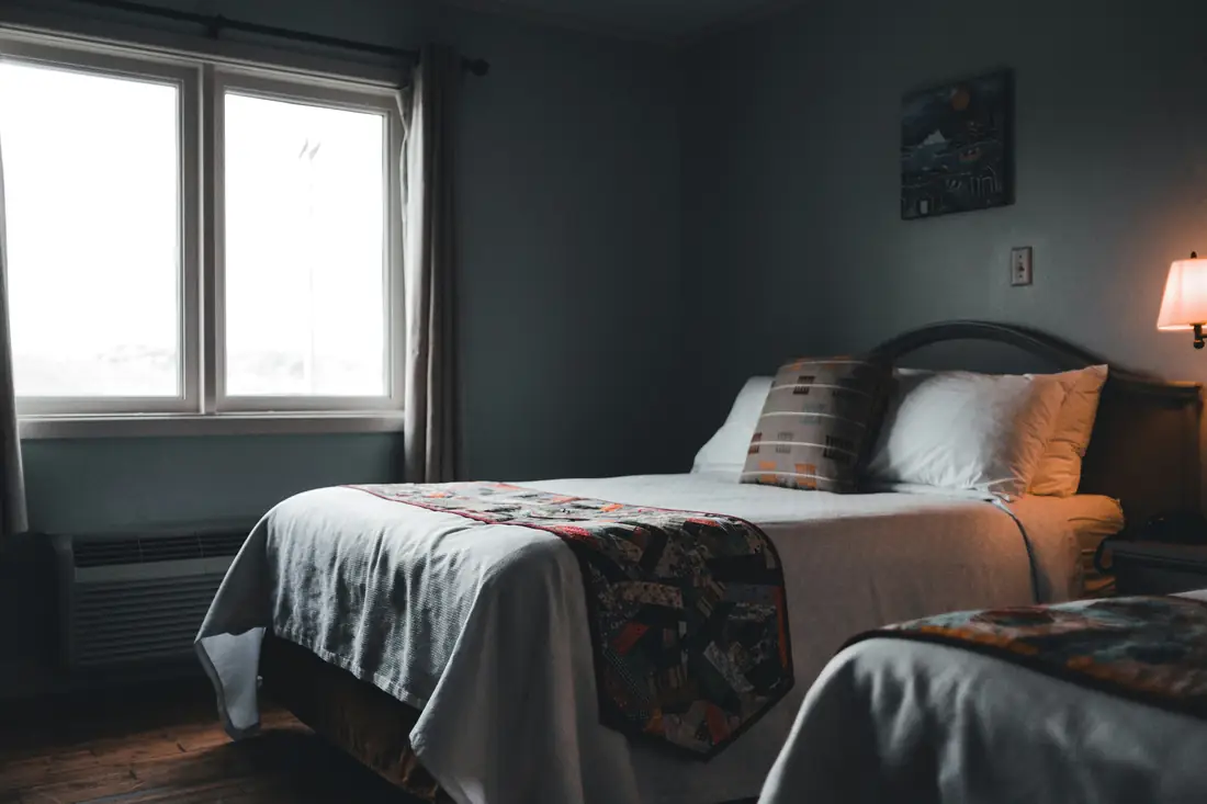 A practical family room with twin beds, soft window light, and warm lamps.