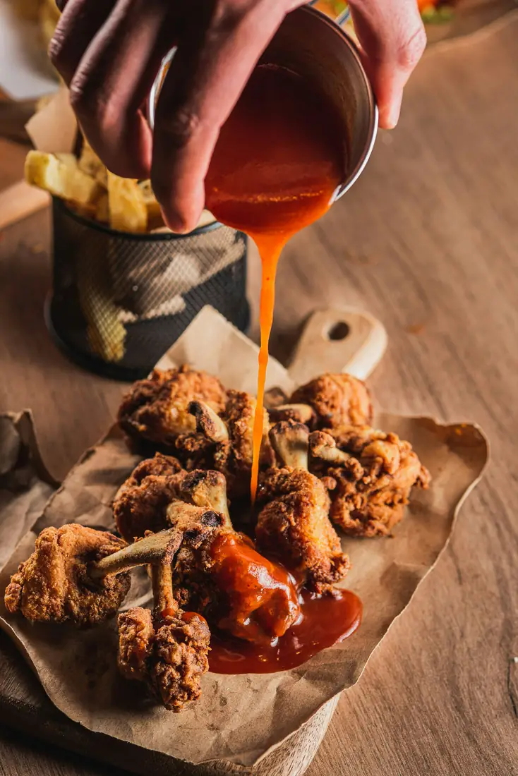 Sauce being poured over fried chicken wings.